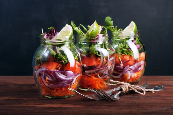 Salát s arugulou, mrkví, rajčaty, purpurovou cibulí a vápnem ve skleněné sklenici. Koncept jídla domácí kuchyně, kterou můžete vzít s sebou do skleněné sklenice. Vegetariánský salát. Užitečná dietní strava. — Stock fotografie