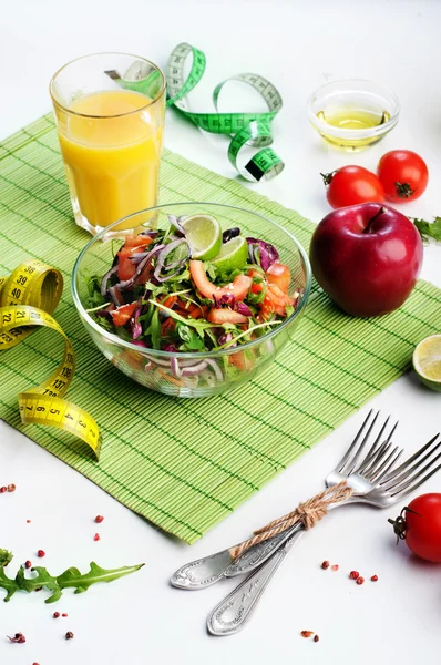 Conceptul de dietă. Salată ușoară de arugula, roșii, ceapă violet și var pe fundal alb. Următoarea bandă de măsurare simbolizează măsurarea volumului corpului în timpul unei diete. Alimente vegetariene cu conținut scăzut de grăsimi . — Fotografie, imagine de stoc
