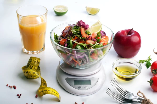 Concept dieet voedsel. Lichte salade van rucola, tomaat, paarse UI en limoen, die staat op de keukenweegschalen.. Volgende meetlint symboliseert meting van lichaams volume tijdens een dieet. Vegetarisch vetarm voedsel. — Stockfoto