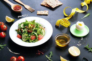 Kavram diyet yiyecek. Roka, salatalık dilimleri ve karanlık bir yüzey üzerinde bir greyfurt salatası. Greyfurt ve yumurta ile klasik diyet bir varyasyonu.