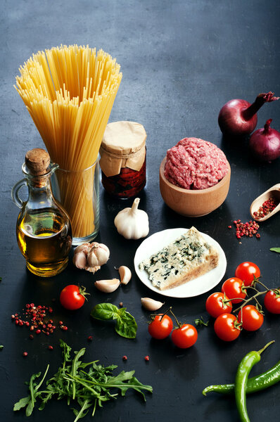 Italian food concept. Ingredients for cooking pasta, such as pasta, onions, tomatoes, olive oil, ground beef, basil leaves and cheese on dark board. Place for writing text
