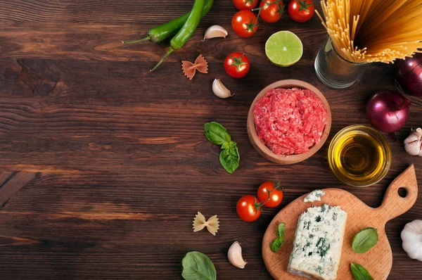 Italian food concept. The paste, cherry tomatoes, ground beef, olive oil, purple onion, half of lime, garlic, basil leaves and a sharp Perey on a brown wooden board. Space for text — Stock Photo, Image