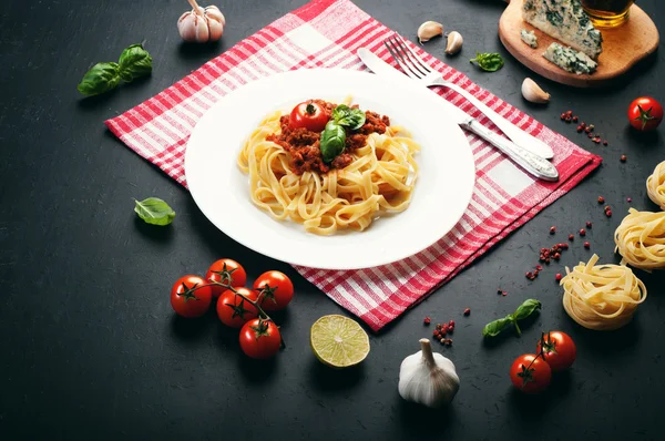 Pasta bolognese in piatto bianco su un tovagliolo bianco e uno rosso. Accanto agli ingredienti per fare la pasta. Cucina Italiana — Foto Stock