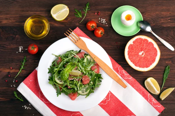 Concepto de dieta de alimentos. La ensalada con la rúcula, los trozos del pepino y el pomelo sobre la superficie oscura. Una variación en la dieta clásica con pomelo y huevos. Fondo de madera marrón — Foto de Stock