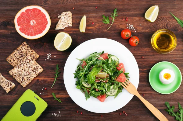 Concept diet food. Salad with arugula, slices of cucumber and a grapefruit on a dark surface. A variation on the classical diet with grapefruit and eggs. Brown wood background — Stock Photo, Image