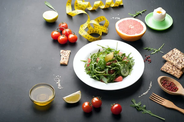 Comida de dieta de conceito. Salada com arugula, partes de pepino e uma toranja em uma superfície escura. Uma variação na dieta clássica com toranja e ovos . — Fotografia de Stock