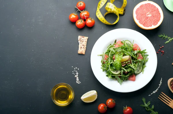 Concetto dieta cibo. Insalata con rucola, fette di cetriolo e un pompelmo su una superficie scura. Una variante della dieta classica con pompelmo e uova . — Foto Stock