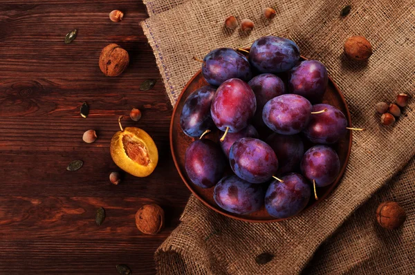 Ameixas suculentas maduras em uma placa de barro em uma superfície de madeira escura. Conceito vegetariano. Frutos sazonais . — Fotografia de Stock