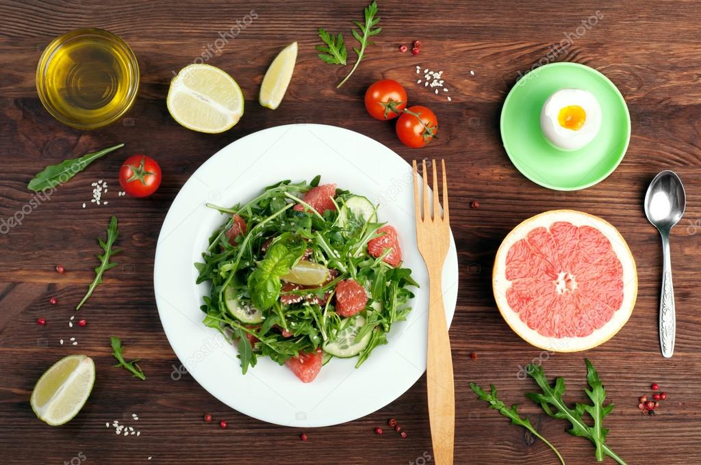 Concept diet food. Salad with arugula, slices of cucumber and a grapefruit on a dark surface. A variation on the classical diet with grapefruit and eggs. Brown wood background