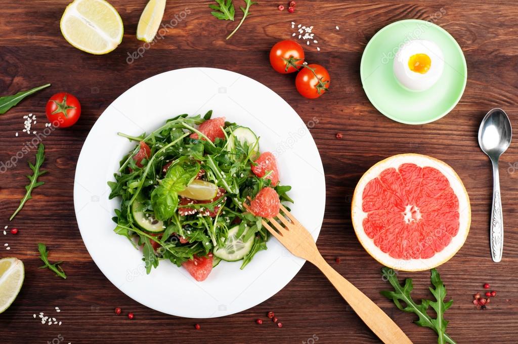 Concept diet food. Salad with arugula, slices of cucumber and a grapefruit on a dark surface. A variation on the classical diet with grapefruit and eggs. Brown wood background