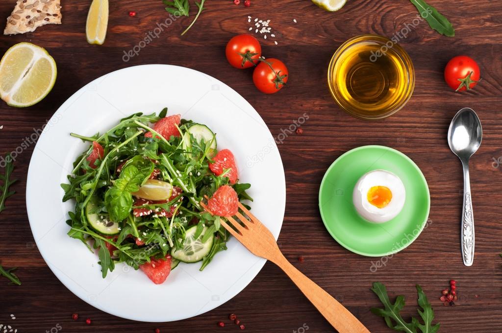 Concept diet food. Salad with arugula, slices of cucumber and a grapefruit on a dark surface. A variation on the classical diet with grapefruit and eggs. Brown wood background