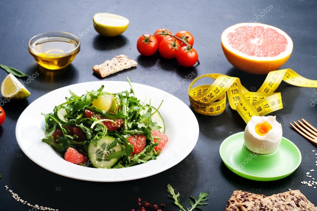 Concept diet food. Salad with arugula, slices of cucumber and a grapefruit on a dark surface. A variation on the classical diet with grapefruit and eggs.