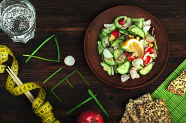 Konsept diyet gıda. Kelime diyet, soğan tüyleri kakma parçaları. Turp ve salatalık, yemek çubukları ve ölçüm bandı ile sonraki bahar salatası. Vegan kavramı.