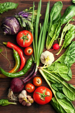 Taze sulu sebze ve otlar, turp gibi, soğan, ıspanak, domates ve acı biber kahverengi bir ahşap tahta üzerinde. Vegan kavramı. Sebze arka plan. 