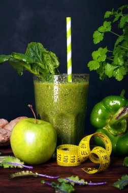 Elma, ıspanak, zencefil ve salatalık ile cam siyah bir zemin üzerine bir bardak taze hazırlanmış bir yüzlü. Çevre sebze ve otlar. Bir vejetaryen diyet kavramı. Düşük kalorili kokteyl hızlı kilo kaybı için