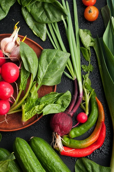 Färska saftiga grönsaker och greener, såsom redish, lök, tomater, spenat, vitlök, kål, kålrabbi, på en mörk yta. Vegetabilisk bakgrund. Vegan Concept. — Stockfoto
