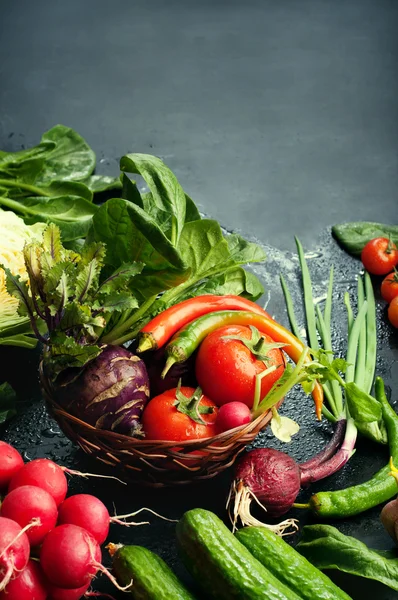 Légumes et légumes verts frais et juteux, tels que le plat rouge, le concombre, les oignons, les tomates, les épinards, l'ail, le chou, le chou-rave, sur une surface sombre. Fond de légumes. Concept végétalien. Place pour le texte — Photo