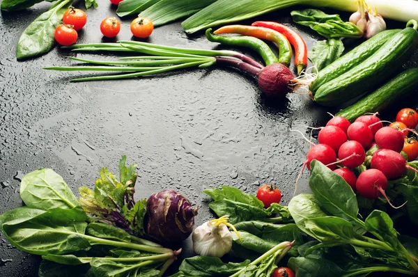 Fresh juicy vegetables and greenery, such as onions, tomatoes, spinach, hot pepper, garlic, cabbage, kohlrabi, and radishes on a black surface. Vegetable background. Vegan concept. Space for text — Stock Photo, Image