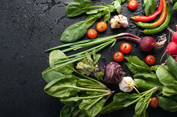 Legumes frescos e suculentos, como cebola, tomate, espinafre, pimenta, alho, repolho, couve-rábano e rabanetes em uma superfície preta. Fundo vegetal. Conceito vegano. Espaço para texto — Fotografia de Stock