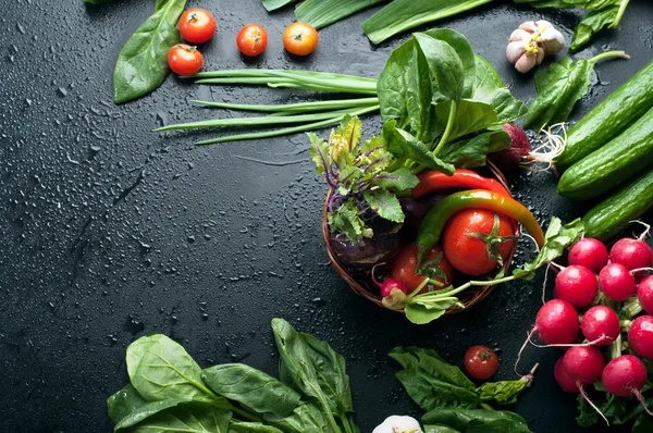 Färska saftiga grönsaker och greener på en svart yta. Plats för att skriva text. Veganskt koncept. Körsbär, gurka, spenat, grön lök, kålkålrabbi, rödaktig och andra — Stockfoto