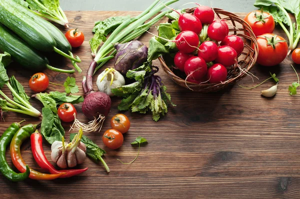 Legumes frescos e suculentos e ervas, como rabanetes, cebola, espinafre, tomates e pimentas em uma tábua de madeira marrom. Conceito vegano. Fundo vegetal. Espaço para texto — Fotografia de Stock