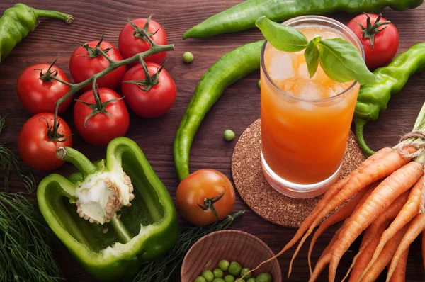 Gemüsesaft mit Eis im Glas auf hölzernem Hintergrund. in der Nähe von Gemüse wie Baby-Karotten, Paprika, Erbsen, Gemüse. das Konzept einer kalorienarmen Ernährung. Bio-Produkte — Stockfoto