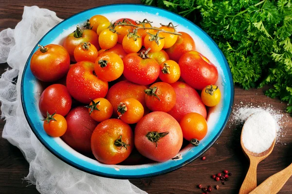 Teller mit Bio-Tomaten in verschiedenen Farben und Größen auf braunem Holzgrund. in der Nähe von Petersilie und Löffel mit Salz. Veganes Konzept. pflanzlicher Hintergrund (Tapete) — Stockfoto