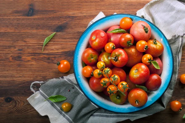 Teller mit Bio-Tomaten in verschiedenen Farben und Größen auf braunem Holzgrund. Veganes Konzept. pflanzlicher Hintergrund (Tapete) — Stockfoto