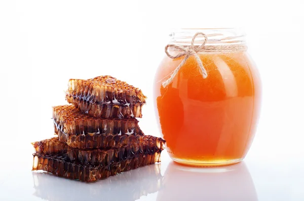 Mel em um jarro de vidro em um fundo branco. Perto do favo de mel. Produto natural da apicultura. Alimentos biológicos — Fotografia de Stock
