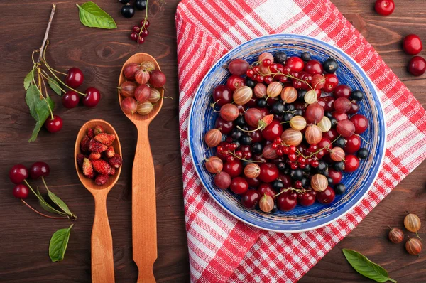 Blue plate with fresh juicy berries such as cherries, gooseberries, strawberries, black and red currants. Concept diet food. Summer berry background (wallpaper)