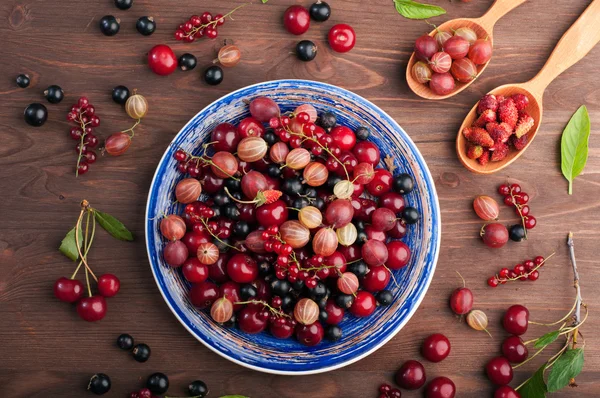 さくらんぼ、グーズベリー、イチゴ、黒と赤スグリなど新鮮なジューシーな果実と青いプレート。コンセプトのダイエット食品。夏のベリー背景 (壁紙) — ストック写真