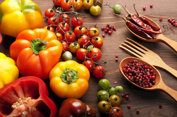 Bio-Lebensmittel-Konzept. frisches, saftiges Gemüse wie Kirschtomaten und bunte Paprika und ein Löffel mit Gewürzen auf braunem Holzgrund. Vegetarische, vegane Produkte. — Stockfoto