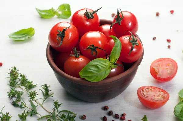 Bright juicy ripe cherry tomatoes in a brown earthenware plate on a white wooden board. Near herbs and spices. Vegan, vegetarian concept