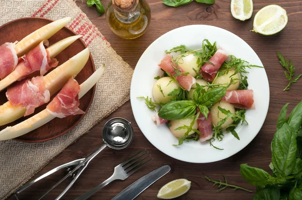 Salada com arugula, bolas de melão e jamon (presunto) em um fundo de madeira marrom. Cozinha espanhola requintada. Tapas. Salada caseira — Fotografia de Stock