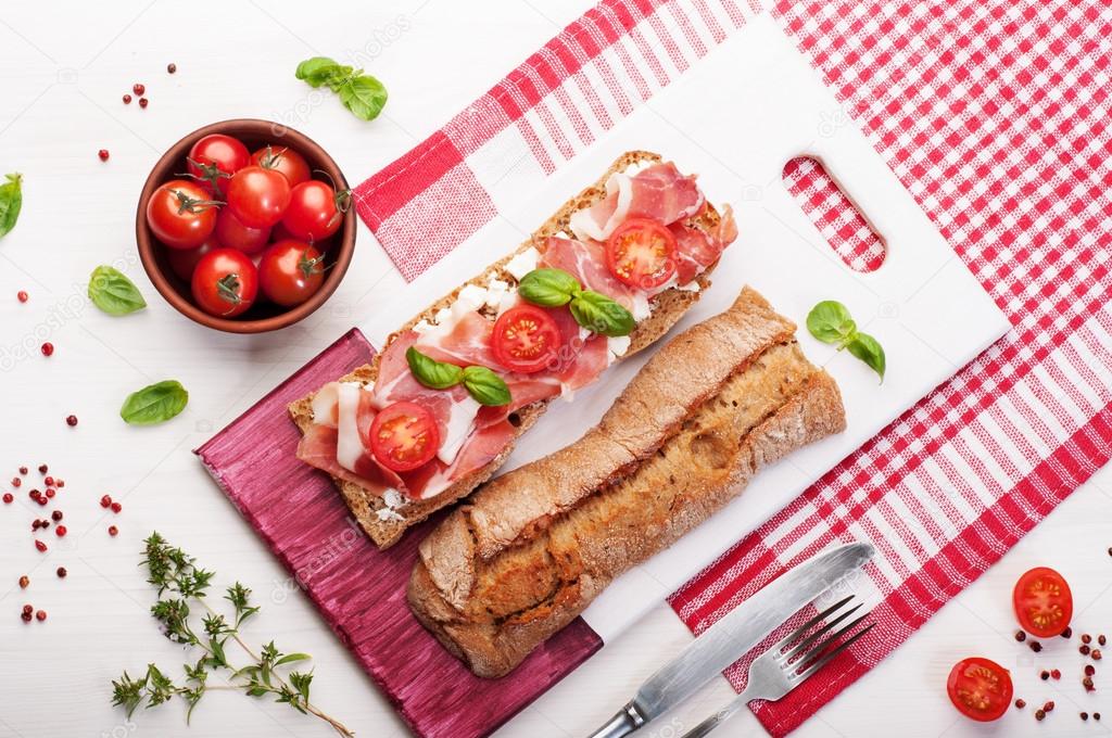 Sandwich of bread with ham, tomato and basil on a wooden cutting board. Useful and tasty lunch that you can take with them to work. Ready-made food