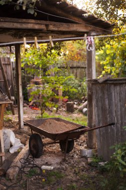 Bahçede inşaat var. Arka planında bir bahçe ve çitin olduğu el arabası..