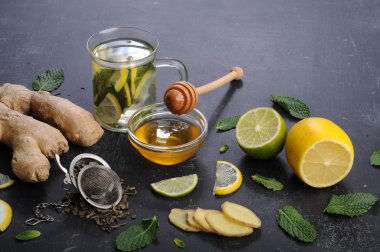 Tea with mint, ginger, lemon and lime on a black background. Next to honey, mint leaves, citrus fruits and tea. The concept of treating colds without pills.