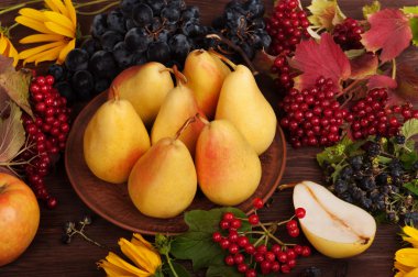 Fresh juicy yellow pears in a clay plate. Near the grass, flowers and autumn fruits. Warm tones. Vegetarian concept