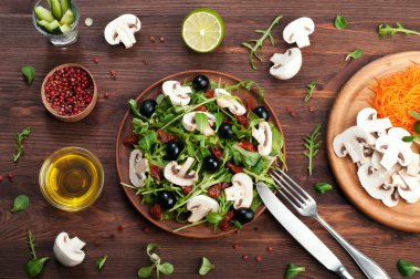 The concept of healthy vegetarian food. Salad with arugula, mushrooms, olives and dried tomatoes. Near spices and olive oil