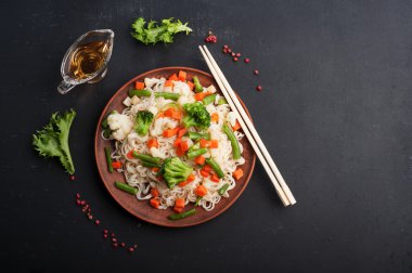 Kahverengi kil bir tabak kızarmış sebze ile yumurta noodles. Baharat ve otlar yanında. Koyu arka plan, arka aydınlatma.