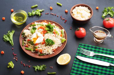 Kahverengi kil bir tabak kızarmış sebze ile yumurta noodles. Baharat ve otlar yanında. Koyu arka plan, arka aydınlatma.