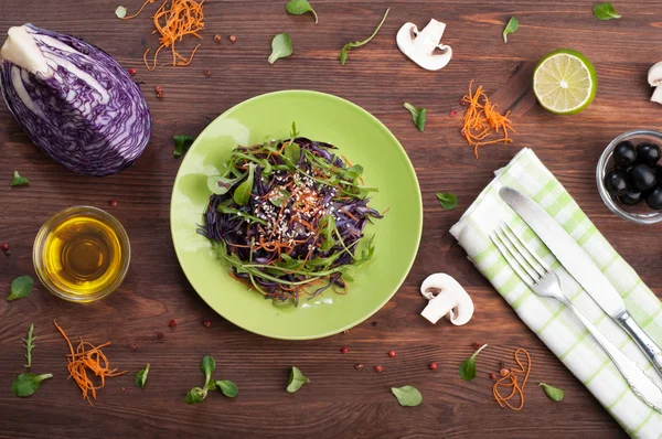 The concept of healthy vegetarian food. Salad with arugula, purple cabbage, carrots and sesame. Beside virgin olive oil, a quarter of cabbage, sliced mushrooms and half lime — Stok fotoğraf