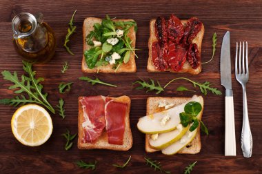 Sandwiches with various fillings, such as arugula, dried tomatoes, pear, blue cheese and ham on wooden background