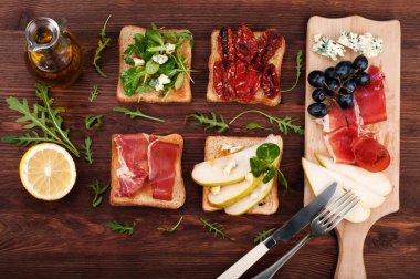 Sandwiches with various fillings, such as arugula, dried tomatoes, pear, blue cheese and ham on wooden background
