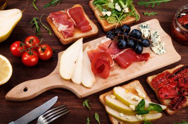 Sandwiches with various fillings, such as arugula, dried tomatoes, pear, blue cheese and ham on wooden background