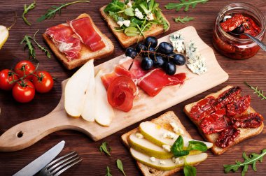 Sandwiches with various fillings, such as arugula, dried tomatoes, pear, blue cheese and ham on wooden background
