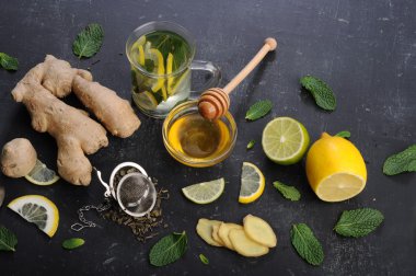 Çay nane, limon, limon ve zencefil karanlık bir arka plan üzerinde. Çay, kıyılmış zencefil kökü gibi için malzemeler yanında nane yaprakları, dilim limon ve kireç. İlaç ve ilaç kullanmaya gerek kalmadan soğuk algınlığı tedavisinde kavramı
