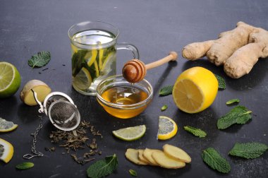 Çay nane, limon, limon ve zencefil karanlık bir arka plan üzerinde. Çay, kıyılmış zencefil kökü gibi için malzemeler yanında nane yaprakları, dilim limon ve kireç. İlaç ve ilaç kullanmaya gerek kalmadan soğuk algınlığı tedavisinde kavramı