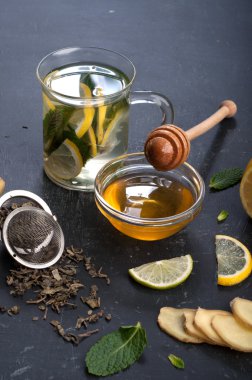 Çay nane, limon, limon ve zencefil karanlık bir arka plan üzerinde. Çay, kıyılmış zencefil kökü gibi için malzemeler yanında nane yaprakları, dilim limon ve kireç. İlaç ve ilaç kullanmaya gerek kalmadan soğuk algınlığı tedavisinde kavramı