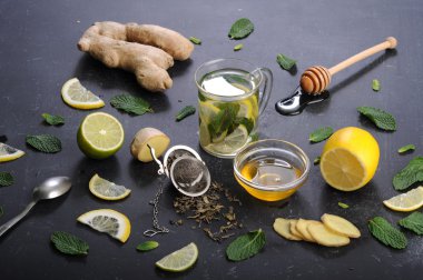 Çay nane, limon, limon ve zencefil karanlık bir arka plan üzerinde. Çay, kıyılmış zencefil kökü gibi için malzemeler yanında nane yaprakları, dilim limon ve kireç. İlaç ve ilaç kullanmaya gerek kalmadan soğuk algınlığı tedavisinde kavramı